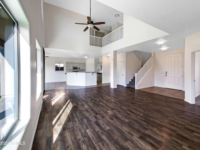 unfurnished living room featuring stairs, a high ceiling, dark wood finished floors, and ceiling fan