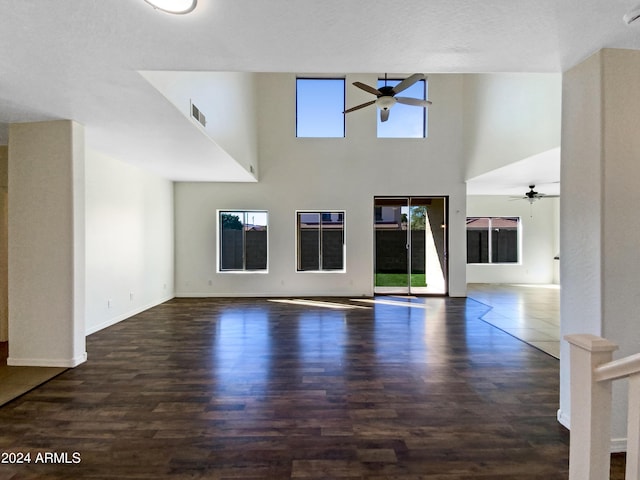 unfurnished living room with visible vents, a ceiling fan, wood finished floors, baseboards, and a towering ceiling