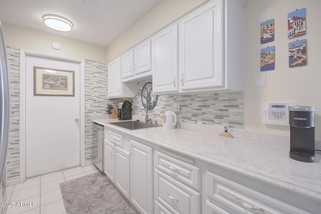 kitchen with dishwasher, sink, light tile patterned flooring, light stone countertops, and white cabinets