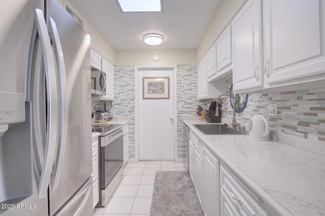 kitchen with white cabinets, appliances with stainless steel finishes, tasteful backsplash, sink, and light tile patterned floors