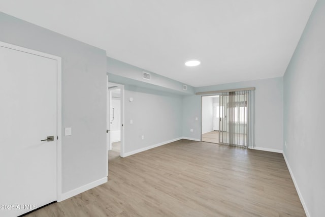 empty room with visible vents, light wood-type flooring, and baseboards