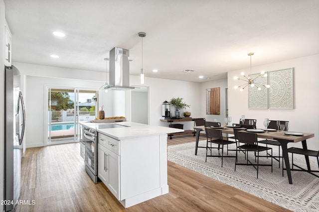 kitchen with pendant lighting, island range hood, white cabinetry, and appliances with stainless steel finishes