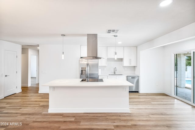 kitchen with sink, wall chimney exhaust hood, stainless steel appliances, hanging light fixtures, and white cabinets