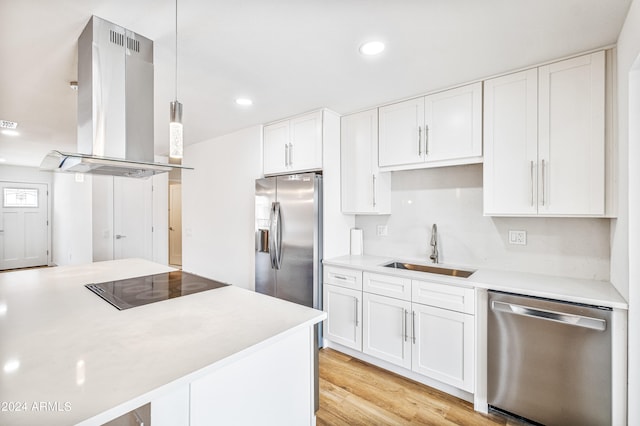 kitchen featuring white cabinetry, sink, decorative light fixtures, island range hood, and appliances with stainless steel finishes