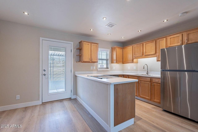 kitchen featuring visible vents, a peninsula, freestanding refrigerator, a sink, and light countertops