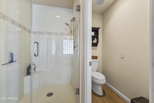 bathroom with hardwood / wood-style floors, a shower with door, and toilet