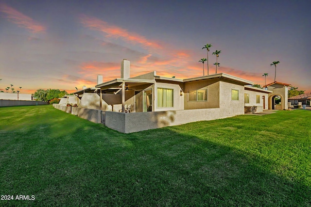 back house at dusk featuring a yard and a patio area