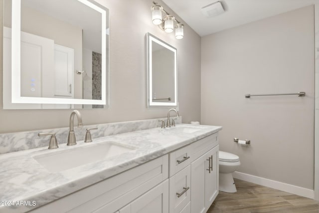 bathroom featuring double vanity, toilet, baseboards, and a sink