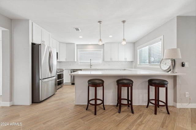 kitchen featuring backsplash, light wood-style flooring, a peninsula, stainless steel appliances, and a sink
