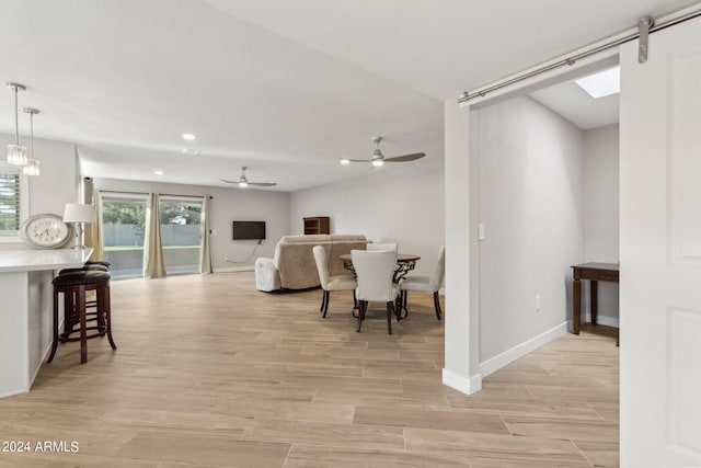 living room with a barn door, a skylight, ceiling fan, and light hardwood / wood-style floors