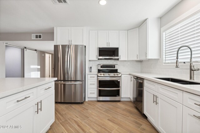 kitchen with white cabinetry, sink, appliances with stainless steel finishes, a barn door, and light hardwood / wood-style floors