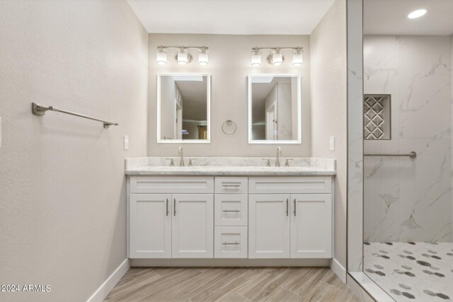 full bath with double vanity, a marble finish shower, baseboards, and a sink