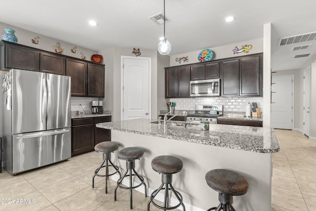 kitchen with a center island with sink, tasteful backsplash, stainless steel appliances, and light stone countertops