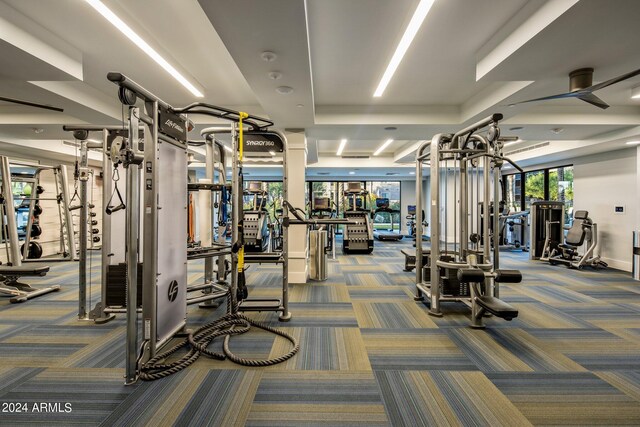 exercise room with decorative columns, carpet flooring, and a raised ceiling