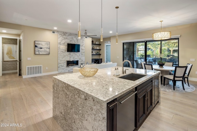 kitchen with light stone counters, sink, stainless steel dishwasher, a large fireplace, and light hardwood / wood-style floors