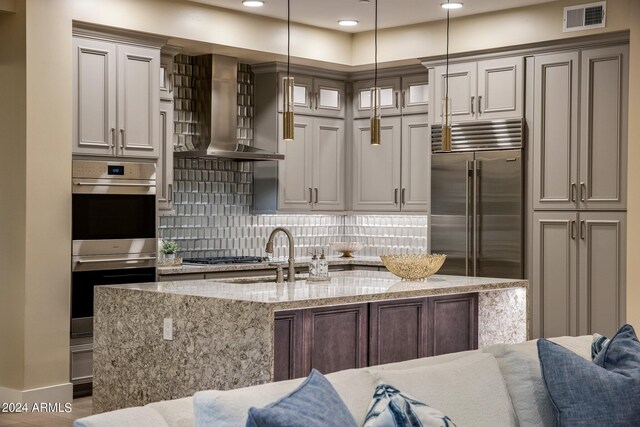 kitchen with light stone counters, backsplash, wall chimney exhaust hood, pendant lighting, and stainless steel appliances