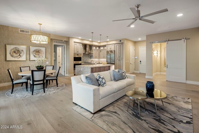 living room featuring ceiling fan with notable chandelier, sink, light hardwood / wood-style flooring, and a barn door