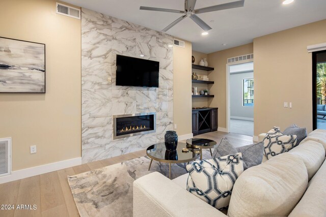 living room with ceiling fan, a fireplace, and light hardwood / wood-style floors