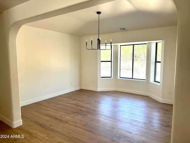 unfurnished dining area featuring a notable chandelier, vaulted ceiling, and dark hardwood / wood-style flooring