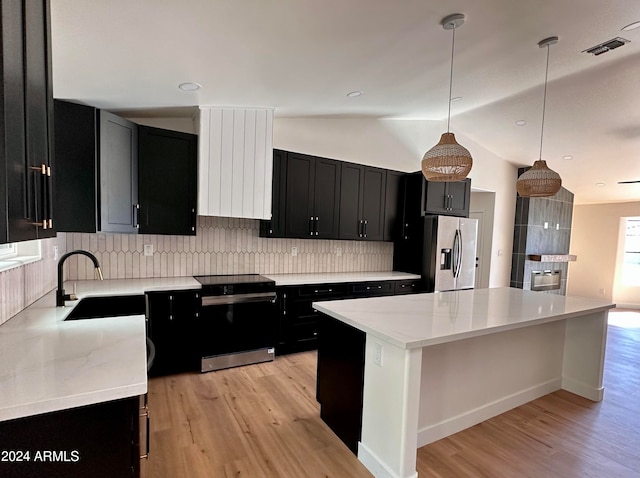 kitchen featuring a kitchen island, hanging light fixtures, stainless steel appliances, vaulted ceiling, and light hardwood / wood-style floors