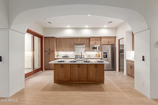 kitchen with light hardwood / wood-style floors, sink, an island with sink, and appliances with stainless steel finishes