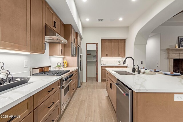 kitchen with sink, stainless steel appliances, light stone counters, light hardwood / wood-style flooring, and a center island with sink