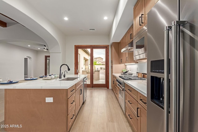 kitchen with ceiling fan, sink, ventilation hood, an island with sink, and high quality appliances