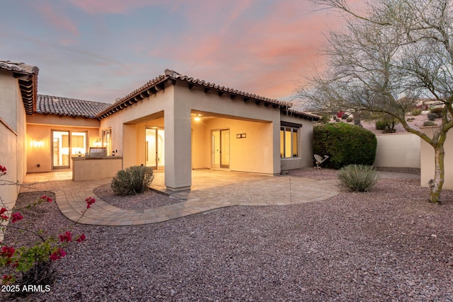 back house at dusk featuring a patio area