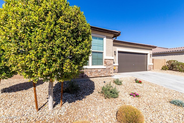 view of front of property featuring a garage, fence, stone siding, concrete driveway, and stucco siding