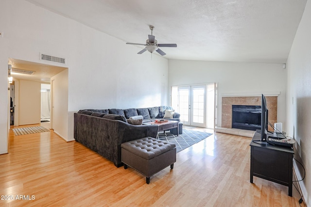 living room featuring hardwood / wood-style flooring, a tile fireplace, high vaulted ceiling, and french doors