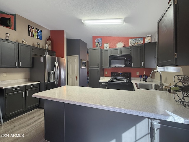 kitchen with kitchen peninsula, a textured ceiling, vaulted ceiling, sink, and black appliances