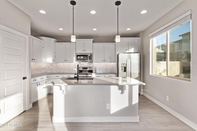 kitchen with white cabinetry, sink, appliances with stainless steel finishes, decorative light fixtures, and an island with sink