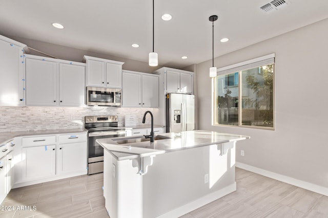 kitchen featuring stainless steel appliances, white cabinets, an island with sink, and decorative light fixtures