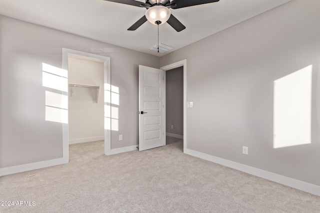 unfurnished bedroom featuring light colored carpet, ceiling fan, a walk in closet, and a closet