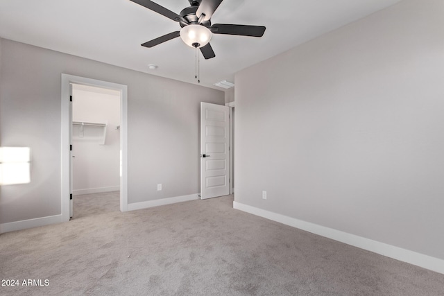 unfurnished bedroom featuring light carpet, ceiling fan, a walk in closet, and a closet