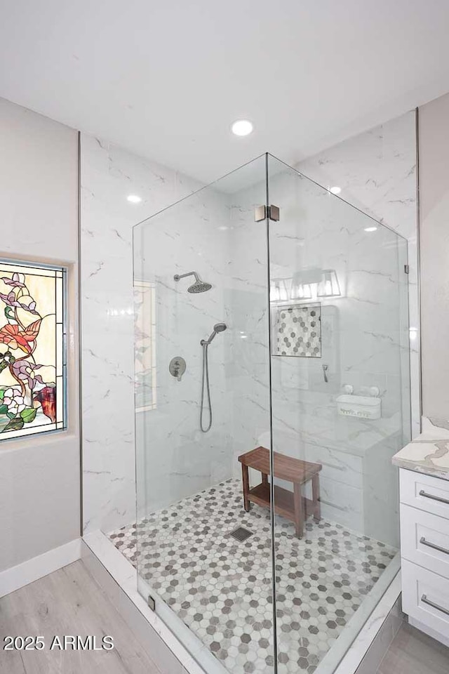 bathroom featuring vanity, wood finished floors, baseboards, and a marble finish shower