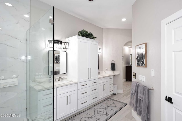 full bathroom featuring a sink, wood finished floors, a marble finish shower, double vanity, and baseboards