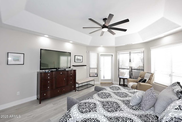 bedroom featuring a tray ceiling, multiple windows, baseboards, and light wood-type flooring