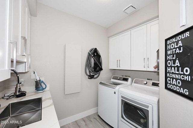 laundry area with light wood-style flooring, washer and dryer, a sink, cabinet space, and baseboards