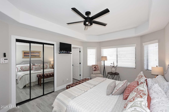 bedroom featuring light wood-style flooring, multiple windows, a raised ceiling, and baseboards