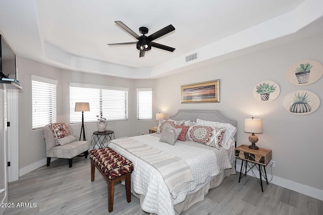 bedroom with visible vents, multiple windows, a raised ceiling, and light wood finished floors