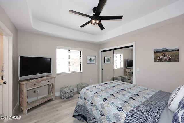 bedroom with a tray ceiling, light wood-style floors, and ceiling fan