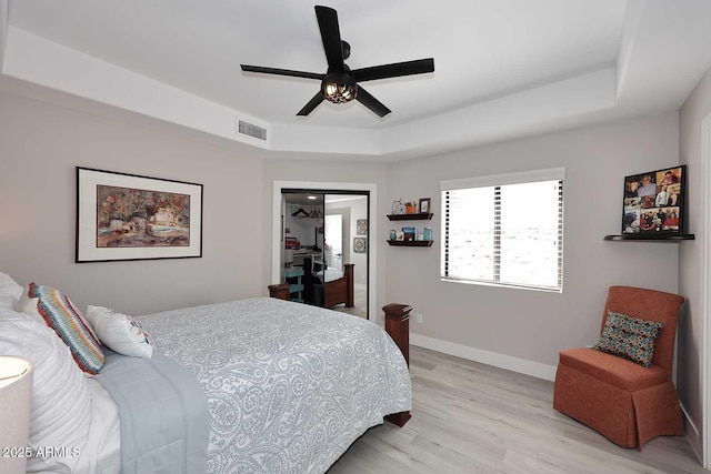 bedroom with a tray ceiling, light wood-style flooring, baseboards, and visible vents