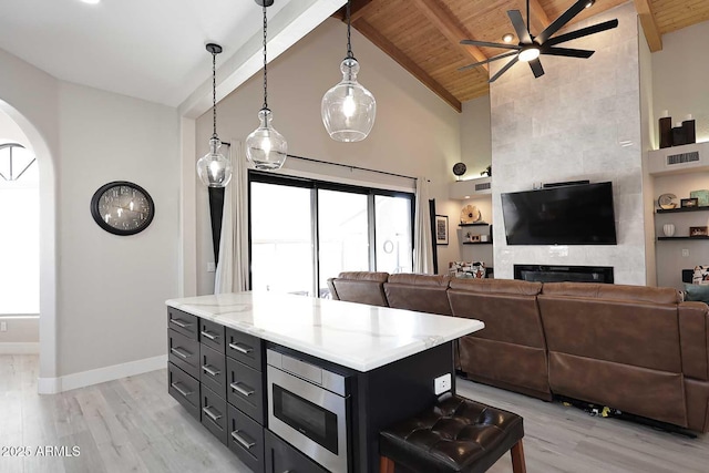 kitchen with baseboards, stainless steel microwave, wooden ceiling, beamed ceiling, and light wood-type flooring