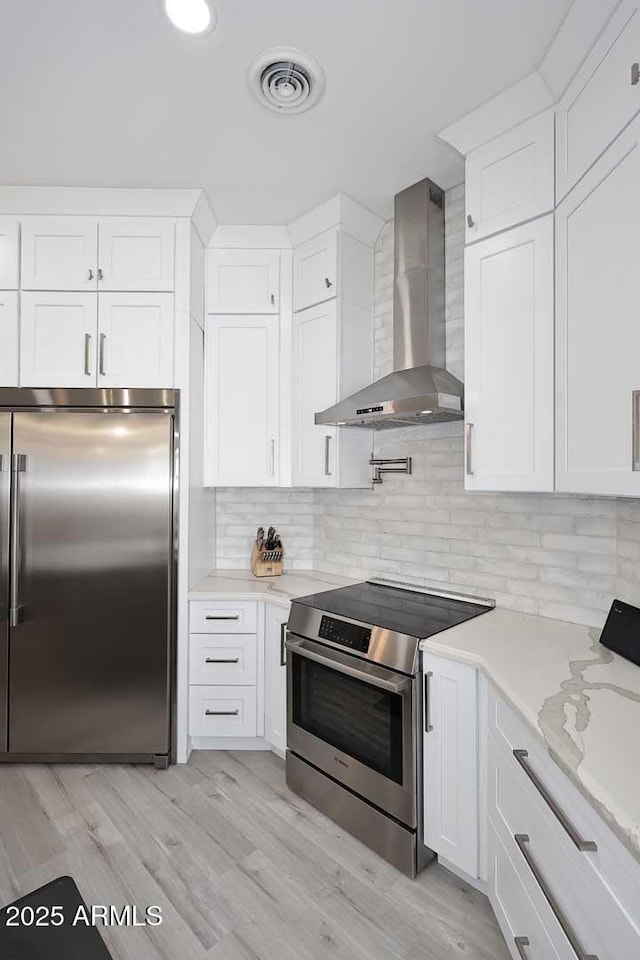 kitchen with visible vents, stainless steel appliances, white cabinets, wall chimney exhaust hood, and backsplash