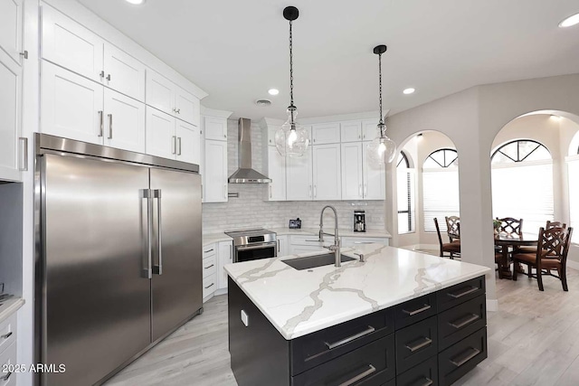 kitchen with a sink, wall chimney range hood, stainless steel appliances, white cabinetry, and dark cabinets