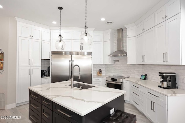 kitchen with a sink, appliances with stainless steel finishes, white cabinets, and wall chimney range hood