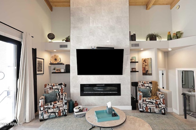 living area featuring beamed ceiling, a fireplace, visible vents, and a towering ceiling