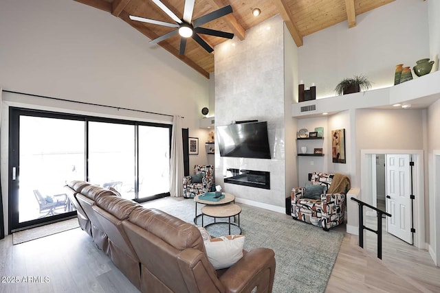 living area featuring beam ceiling, light wood-style flooring, wooden ceiling, a fireplace, and high vaulted ceiling