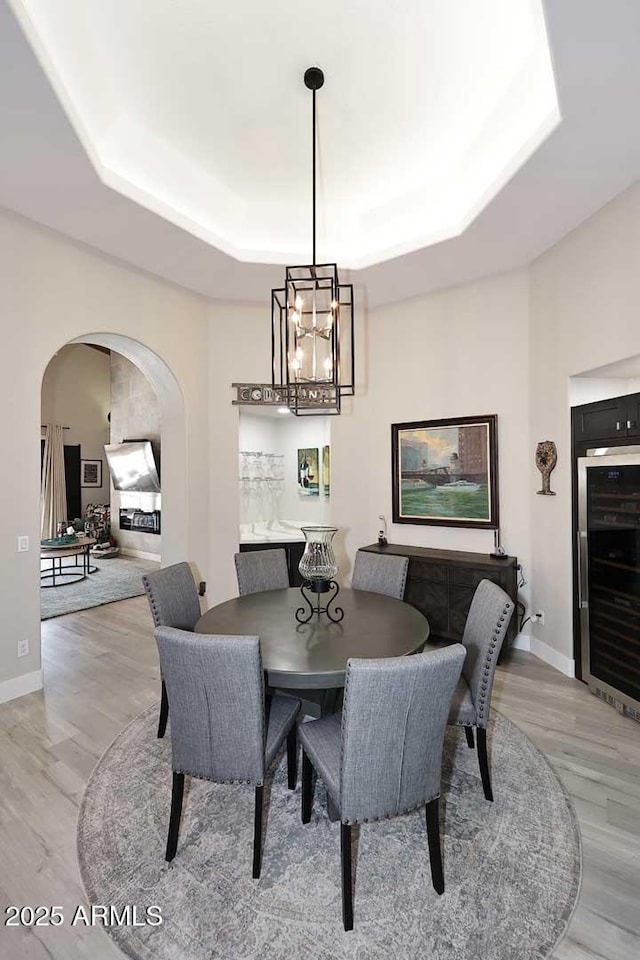 dining room featuring a tray ceiling, baseboards, arched walkways, and light wood-type flooring